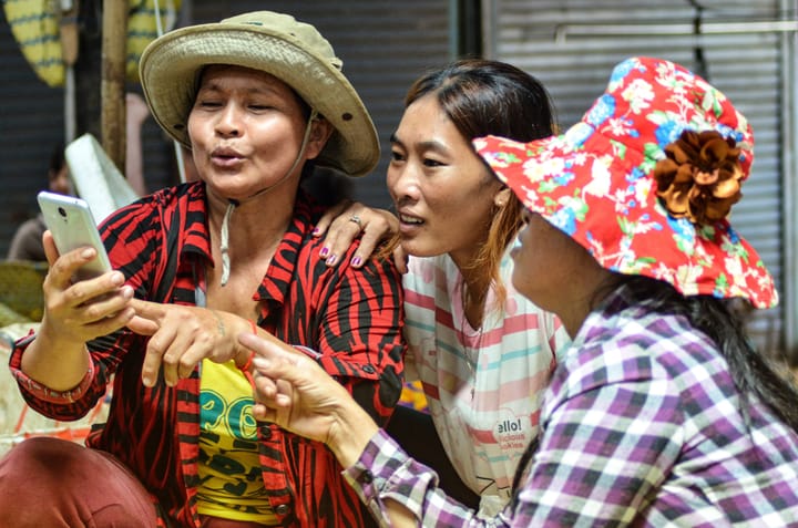 Cambodian women at a market, looking at a smartphone.